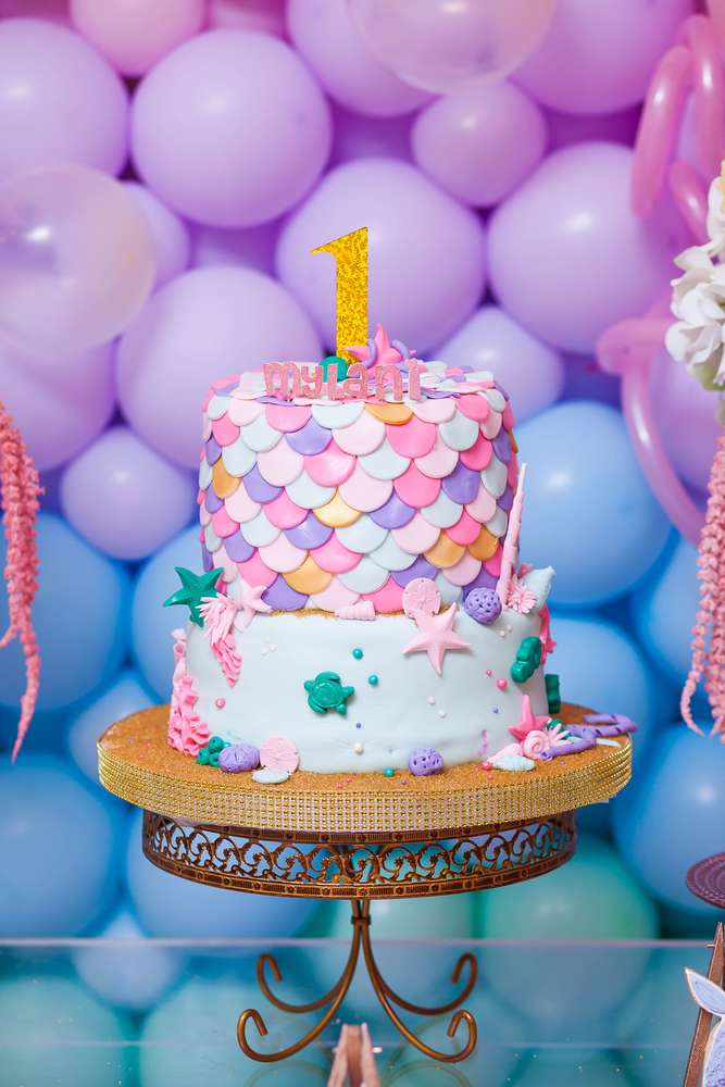 Under the Sea 1st birthday party I CatchMyParty.com Under the sea tiered birthday party with a top tier decorated with pink, purple, gold and turquoise mermaid tail scales and a bottom tier decorated with under the sea motifs