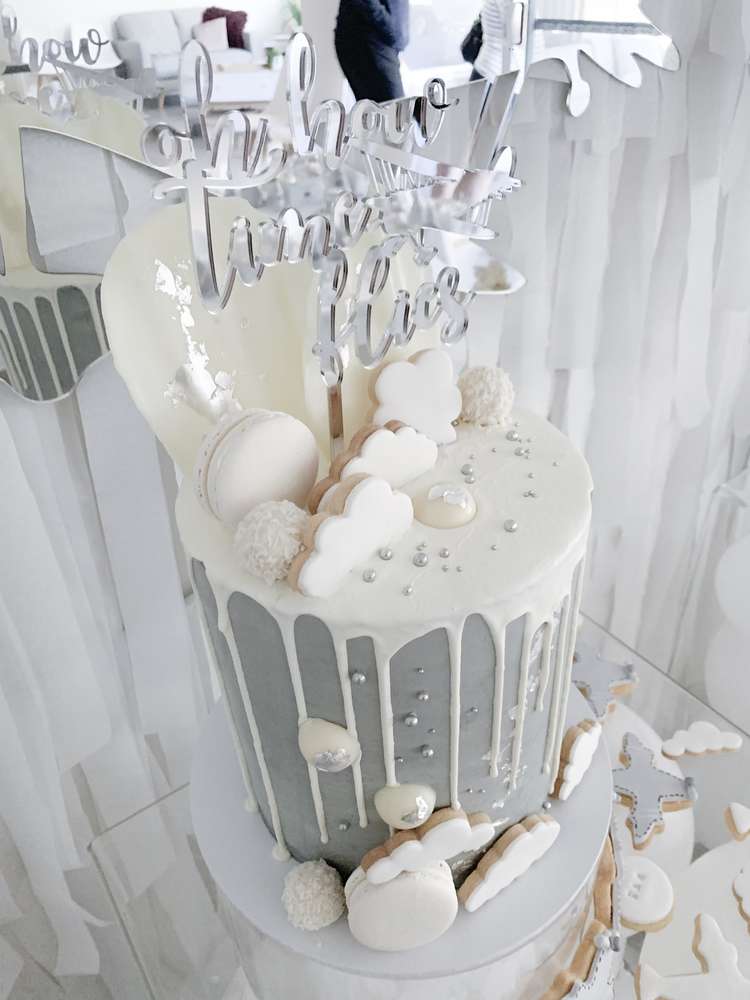 The incredible grey birthday cake with white dripped iced, topped with a mix of white cloud cookies, macarons, coconut cake pops, silver sprinkles, and topped with a mirrored 'Oh now times flies' cutout topper