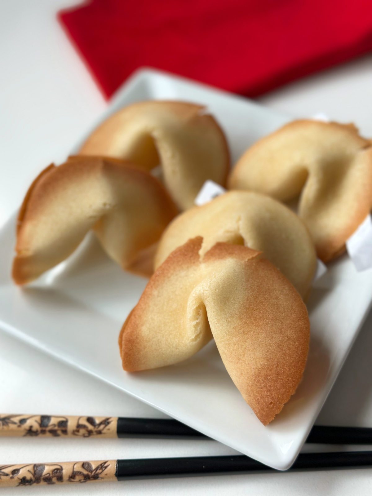Five fortune cookies on a plate with chopsticks.